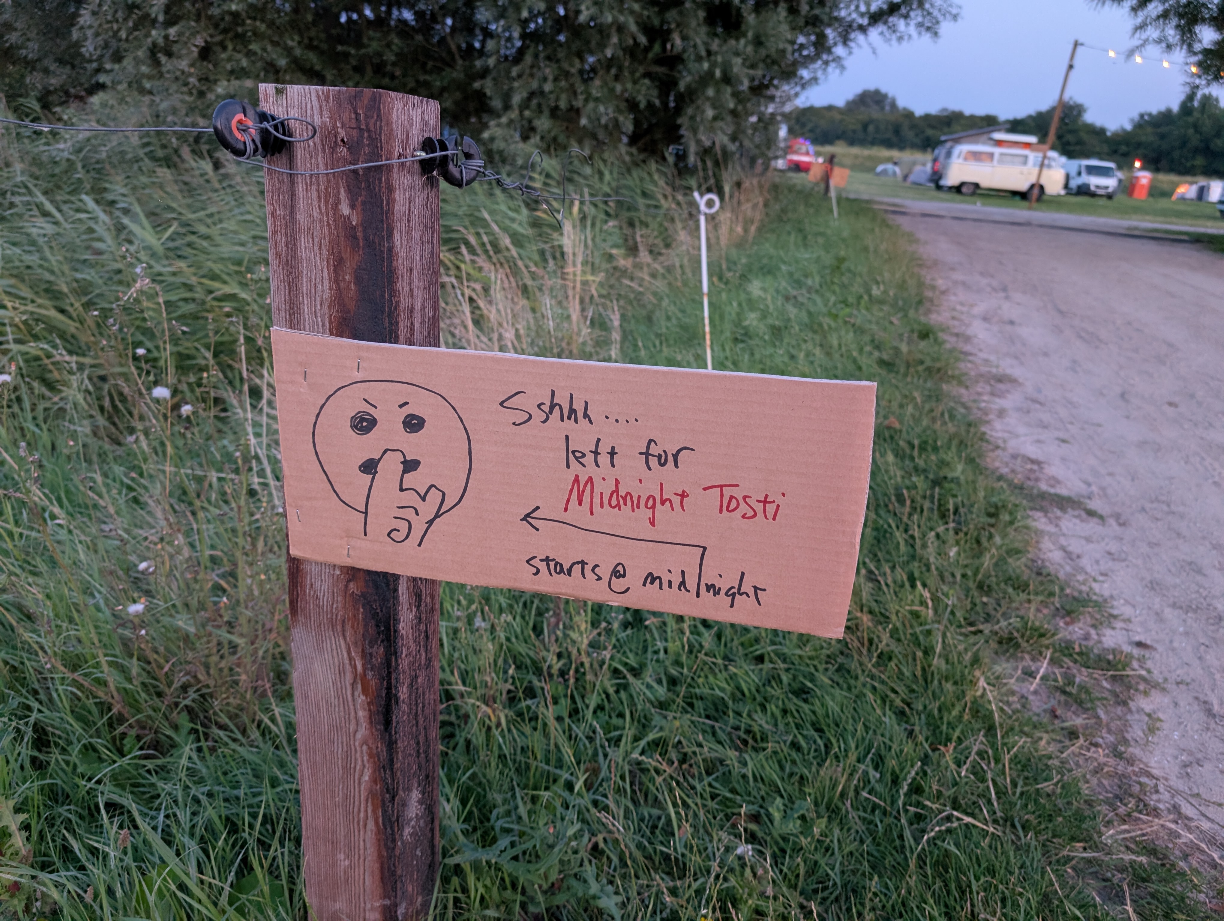 a hand-lettered cardboard sign with a hand drawn "quiet" emoji is attached to a wood post. the text says "Sshhh... left for midnight tosti"